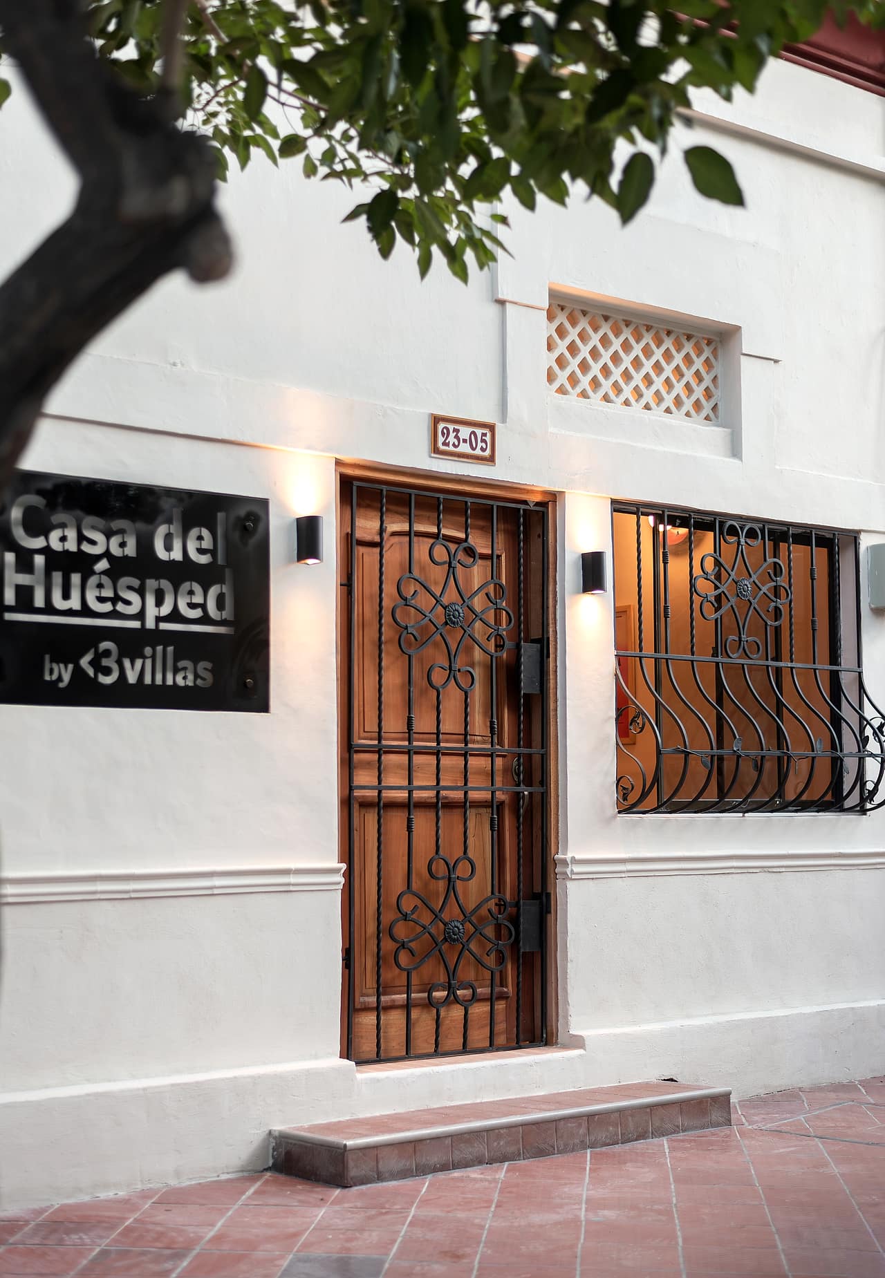 Fachada blanca de La Casa del Huésped con reja de hierro forjado y puerta de madera